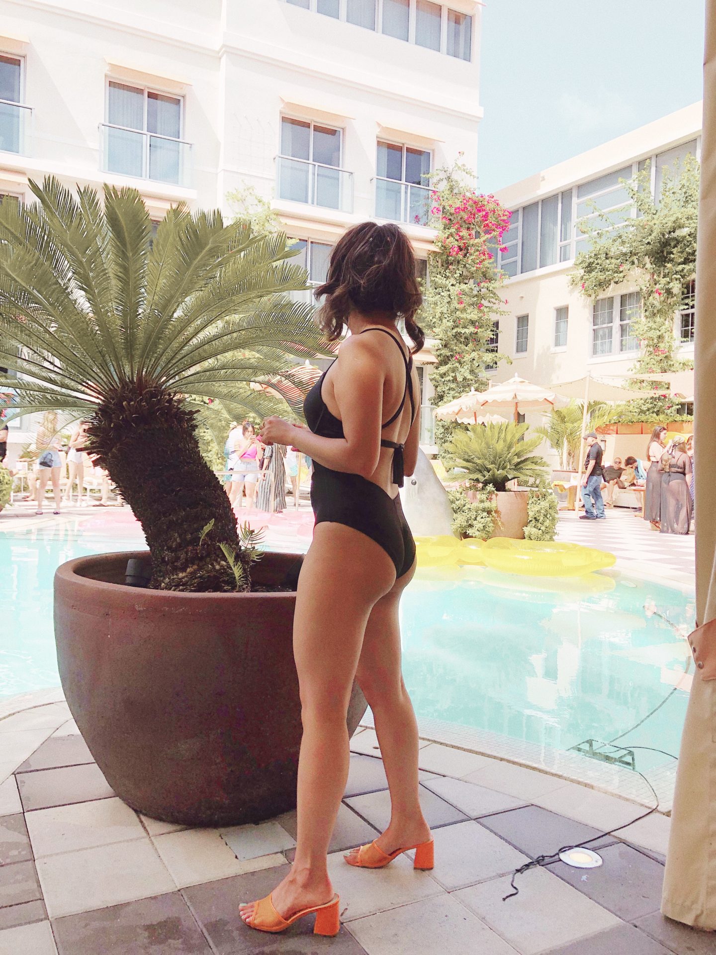 Lounging poolside with a classic black one piece swimsuit from Adore Meand orange mules 