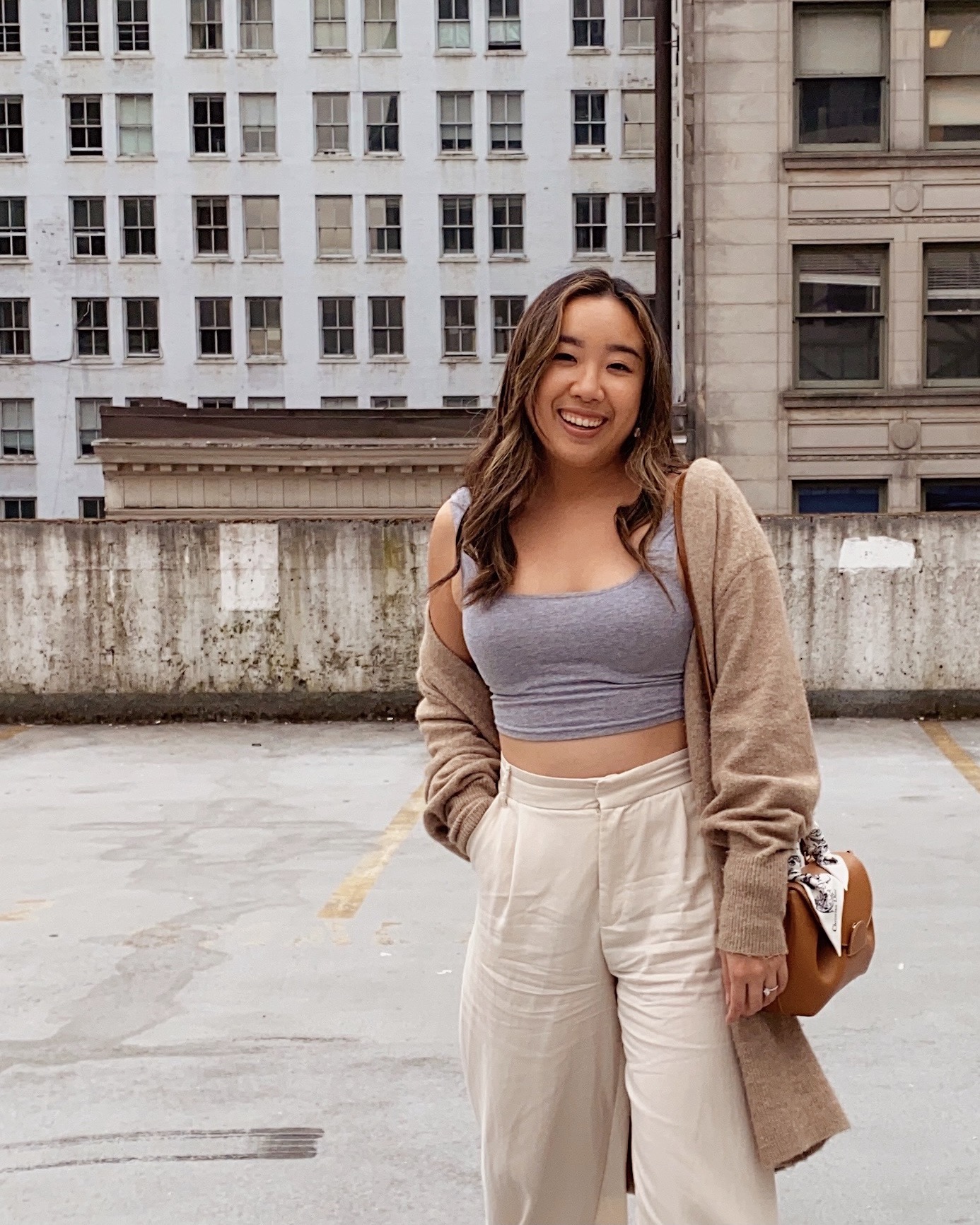 Smiling girl with light brown cardigan and white biege pants paired with leather brown bag for fall 