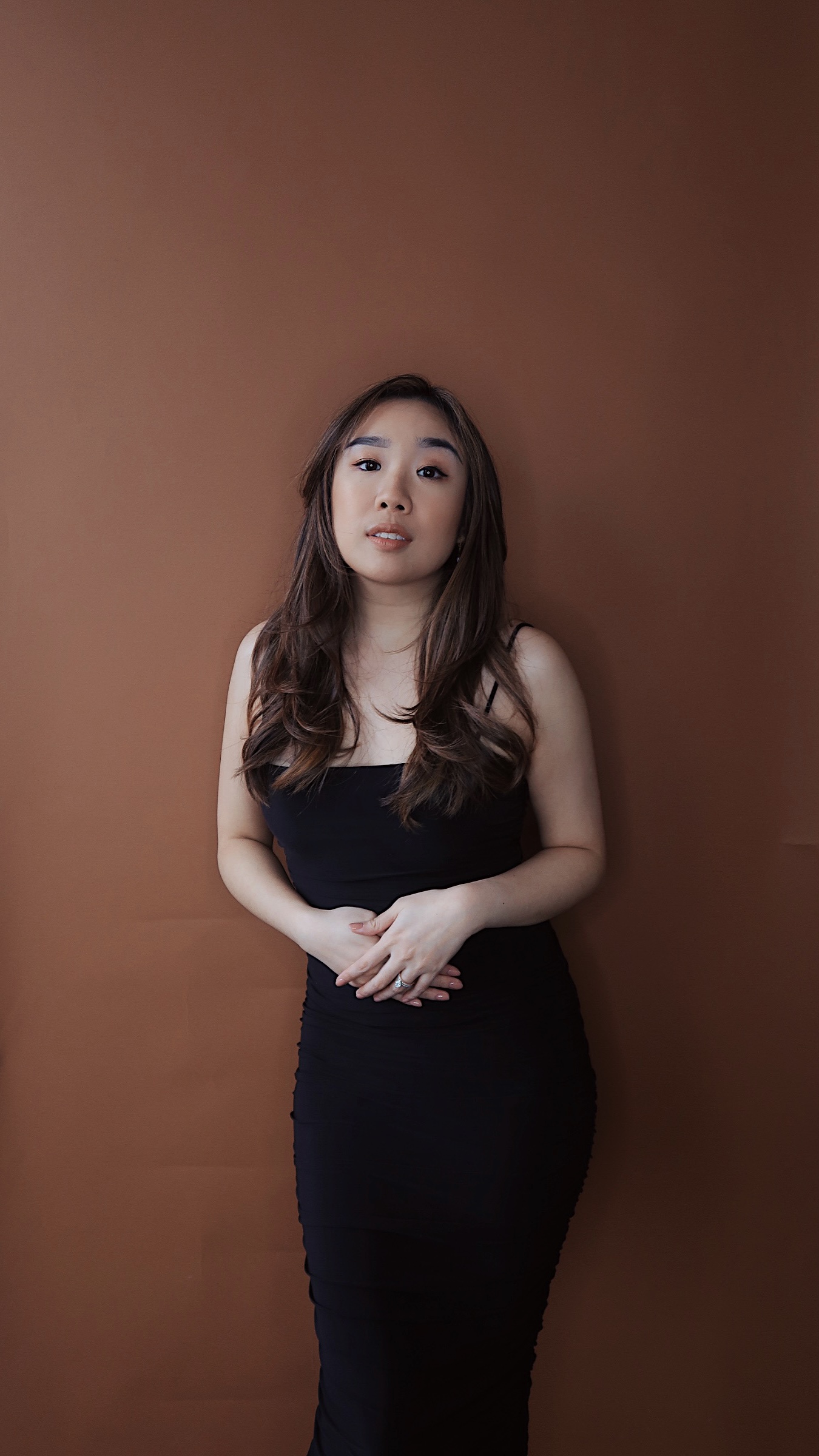 Woman standing in front of a brown background in a black dress